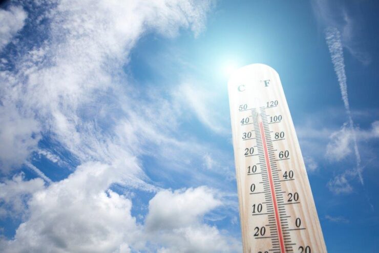 Tall-thermometer-standing-against-a-blue-sky-with-clouds-backdrop