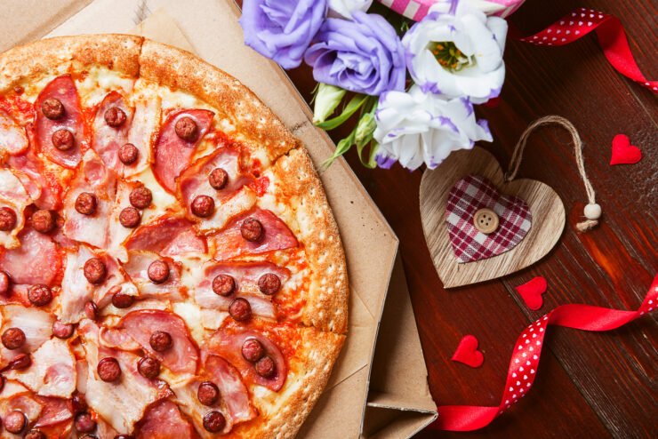 food-pr-shot-of-meat-pizza-next-to-flowers-and-wooden-heart-ornament