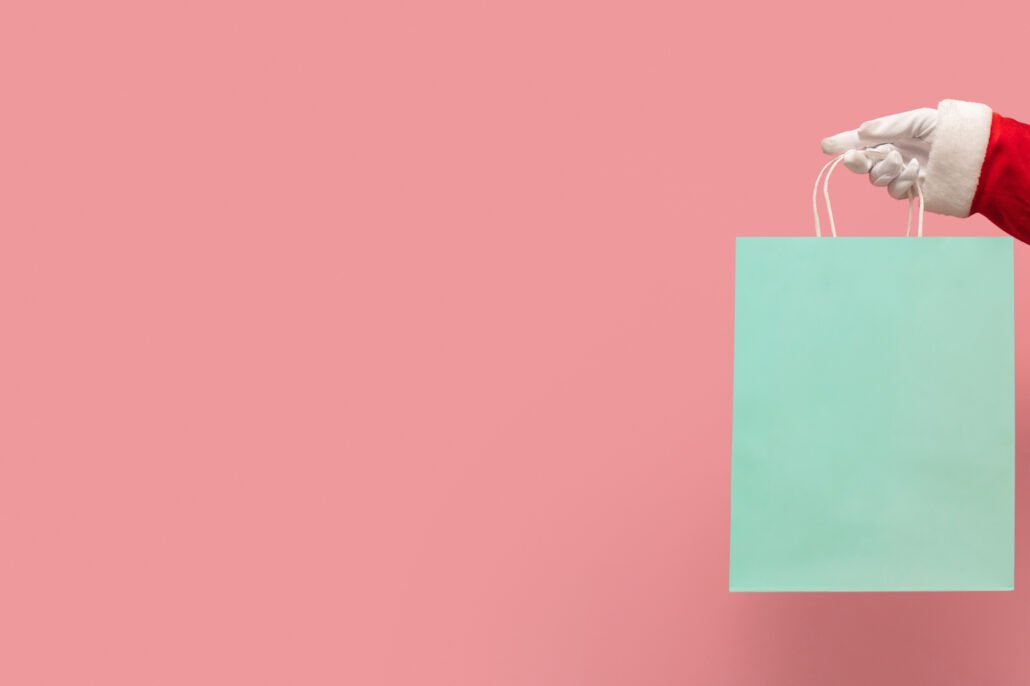 santa-claus-hand-holding-blue-shopping-bag-on-isolated-pink-background