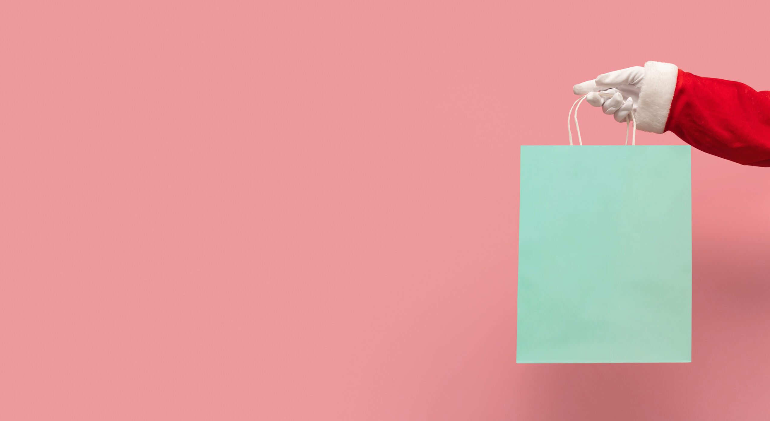 santa-claus-hand-holding-blue-shopping-bag-on-isolated-pink-background
