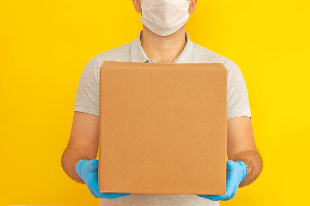 delivery-man-holding-cardboard-boxes-in-medical-rubber-gloves-and-mask-on-yellow-background