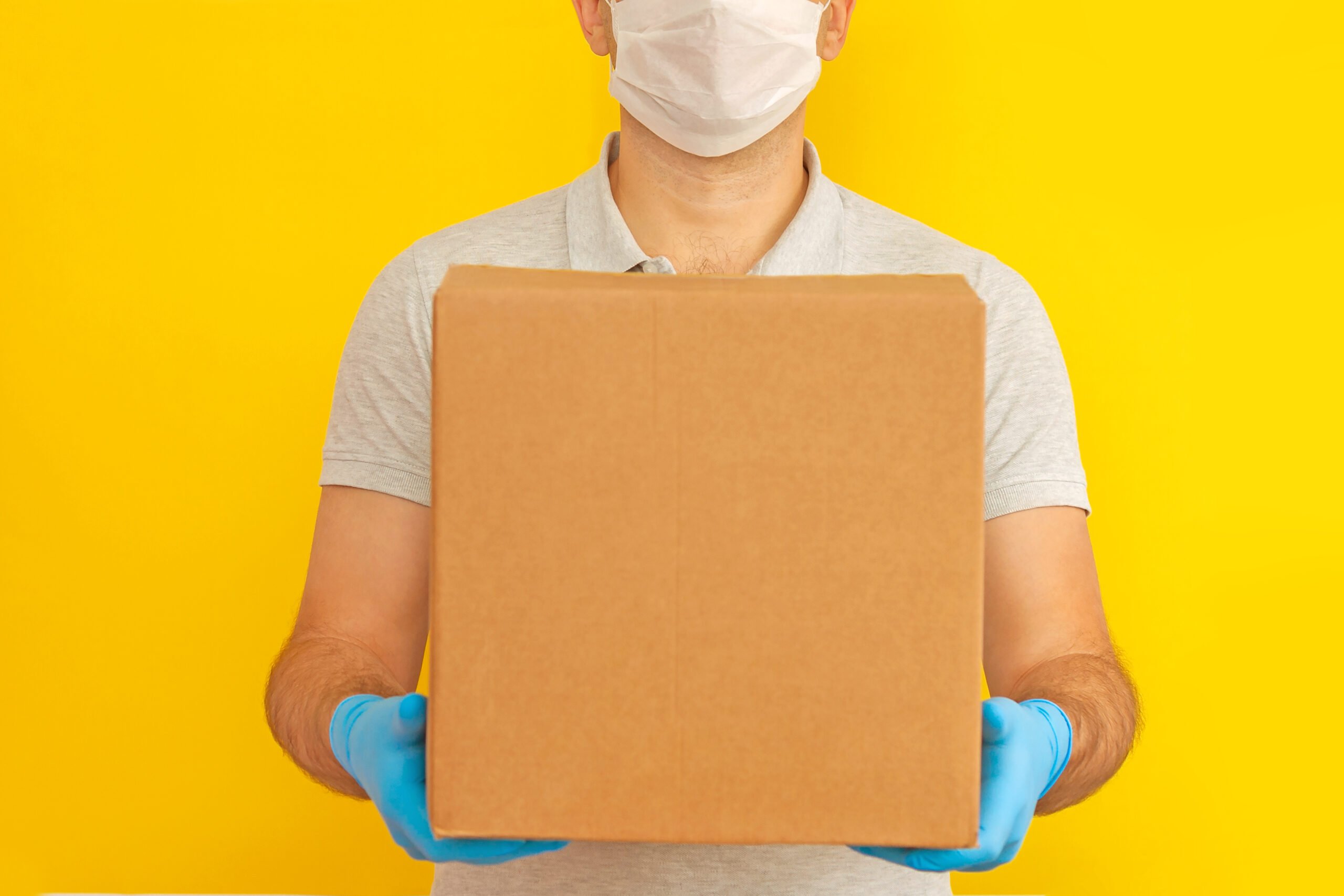 delivery-man-holding-cardboard-boxes-in-medical-rubber-gloves-and-mask-on-yellow-background