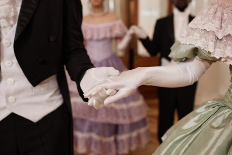 Close-up-of-regency-lady-and-gentleman-holding-hands-wearing-gloves-entering-ballroom