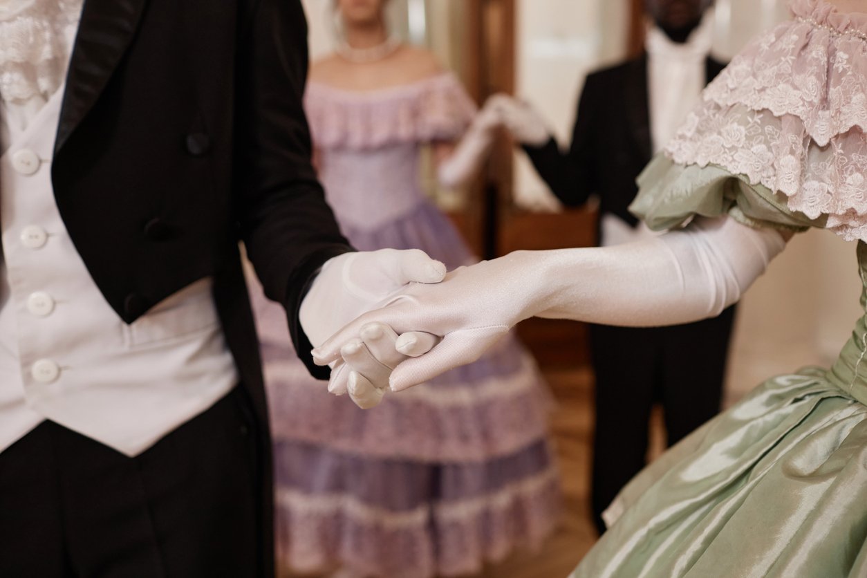 Close-up-of-regency-lady-and-gentleman-holding-hands-wearing-gloves-entering-ballroom