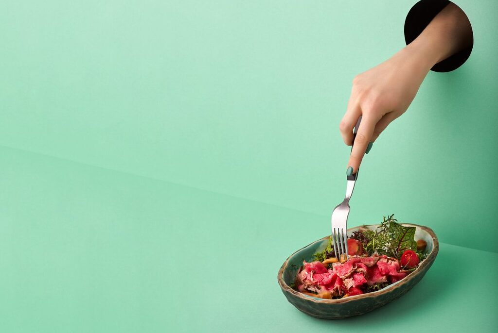 hand-through-hole-in-wall-reaching-down-with-fork-to-a-plate-of-food