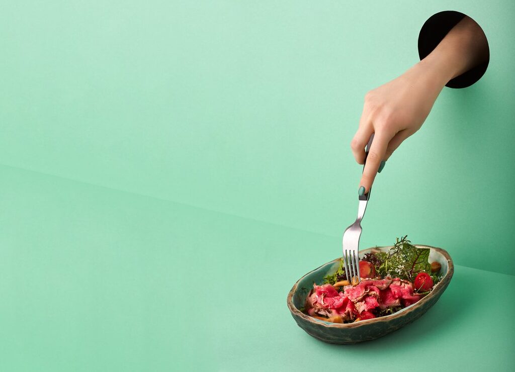 hand-through-hole-in-wall-reaching-down-with-fork-to-a-plate-of-food