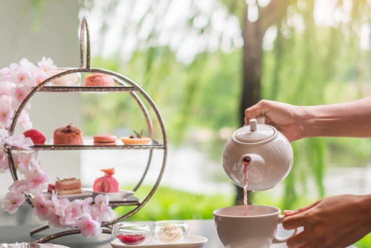 Woman-hand-pouring-hot-tea-with-Afternoon-tea-set-and-Pink-dessert-at-luxury-hotel