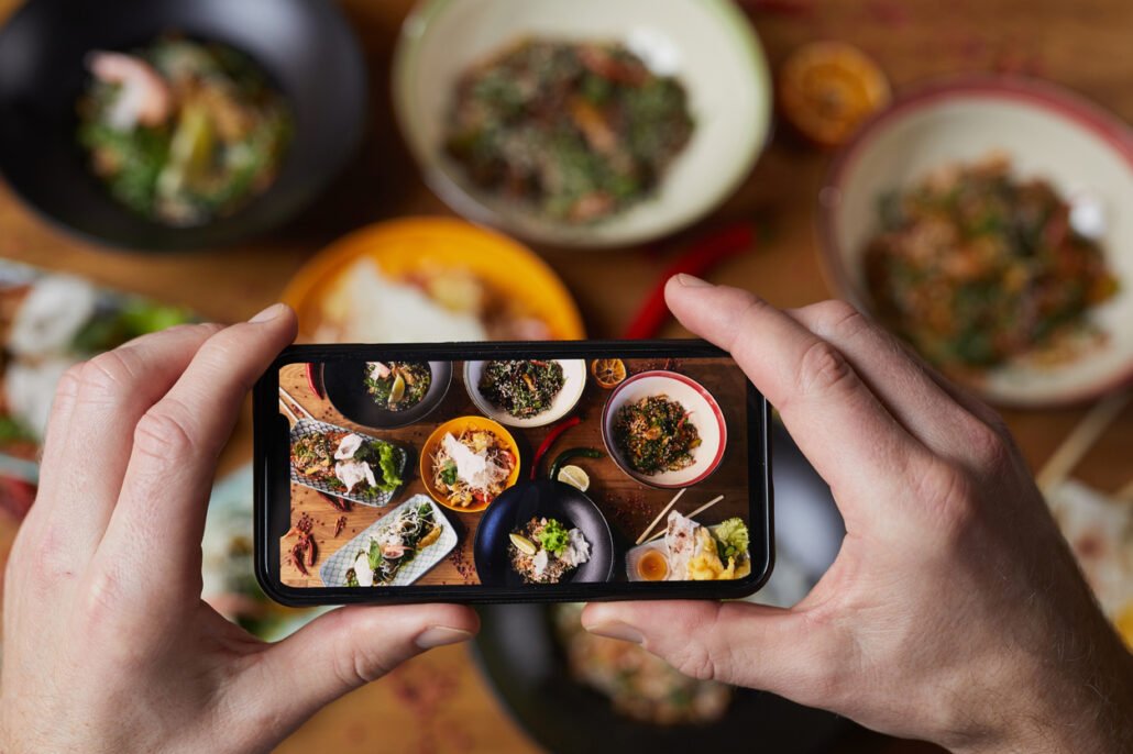 Close-up-of-hands-taking-photo-of-plates-of-food-focus-on-smartphone-screen