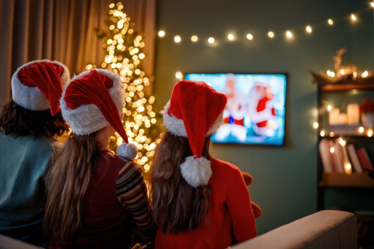 Family-watching-Christmas-Adverts-at-home-on-television-indoors-next-to-Christmas-tree
