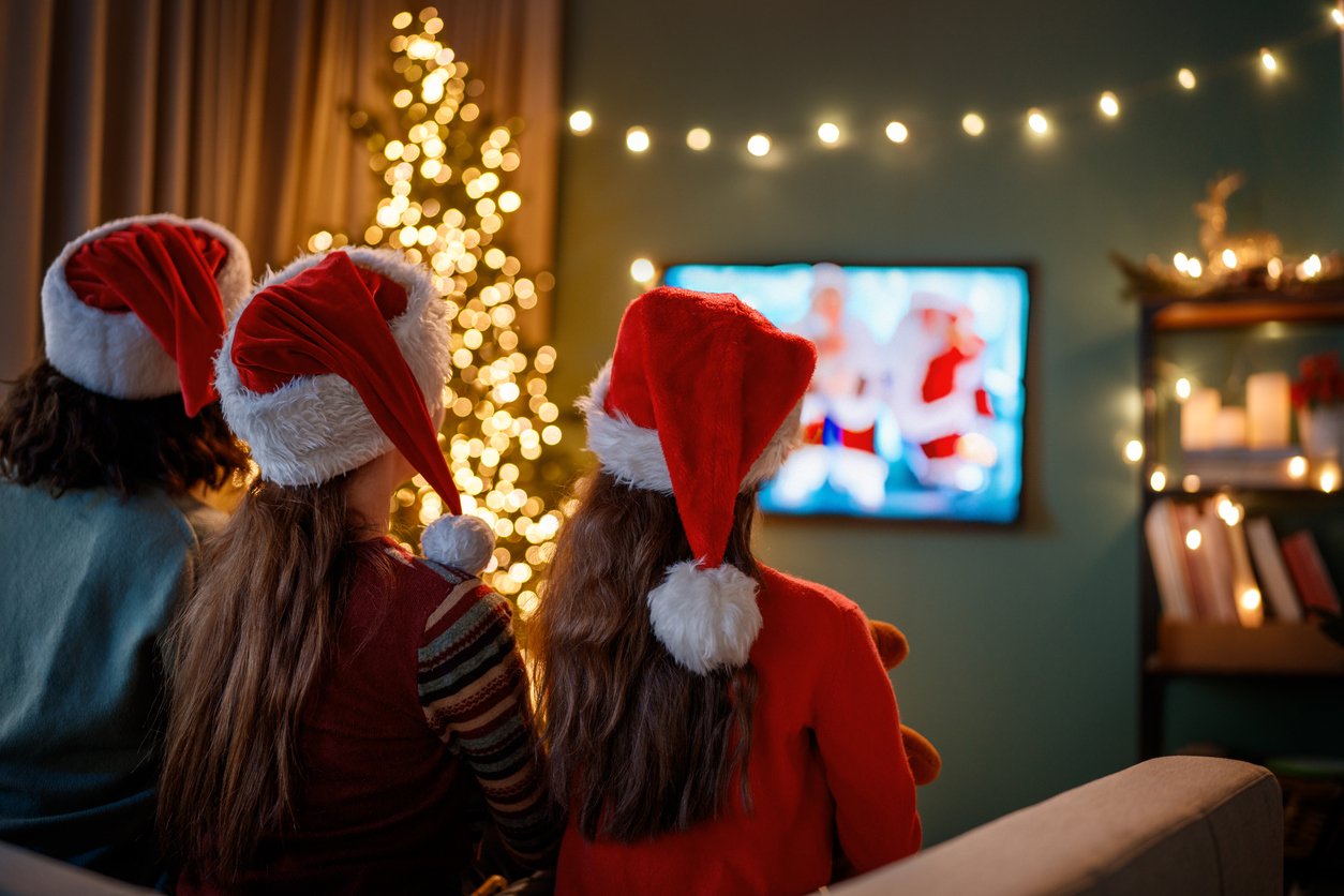 Family-watching-Christmas-Adverts-at-home-on-television-indoors-next-to-Christmas-tree