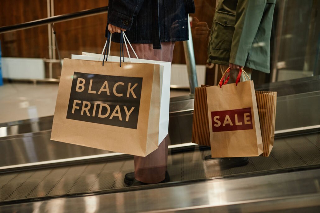 Cropped-shot-of-unrecognizable-couple-holding-shopping-bags-with-Black-Friday-sale-sign-while-standing-at-escalator-in-mall