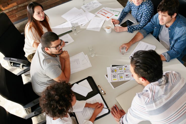 High angle view of creative team sitting around table discussing business ideas. Mixed team of full-service agency professionals meeting in conference room.